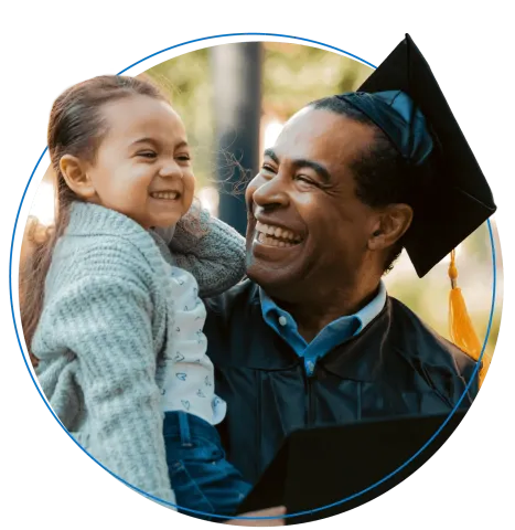 Graduating dad wearing a cap and gown smiles while holding daughter.